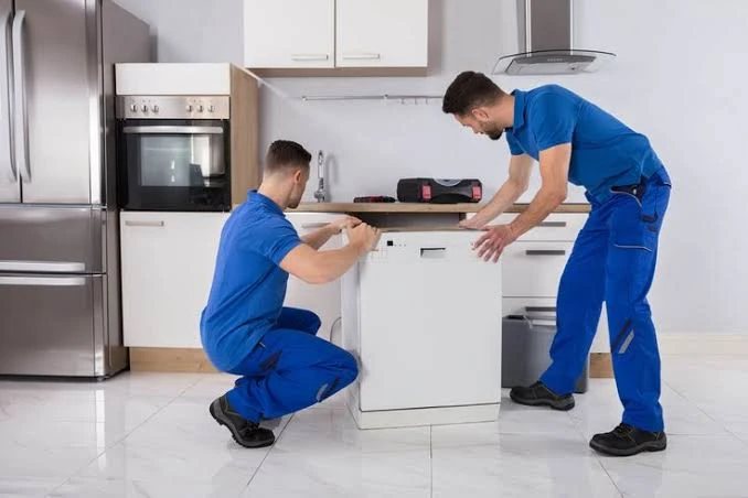 Two technicians positioning a dishwasher in a home kitchen