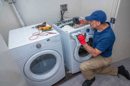 Technician working on a front-loading washing machine beside a dryer