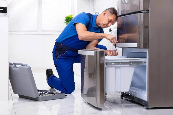 Technician servicing the lower drawer of a stainless steel refrigerator